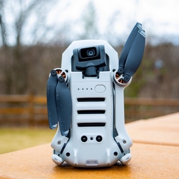 Picture of a small robot on a table outdoors that looks kind of like r2d2 from star wars and is cutely waving maybe.