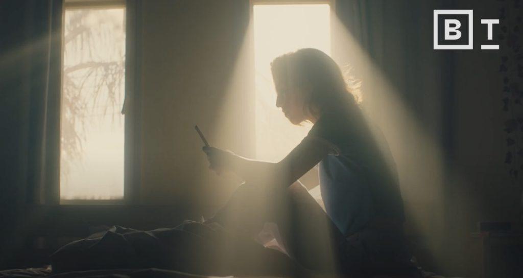 A woman is glued to her phone, sitting in bed during the daytime.